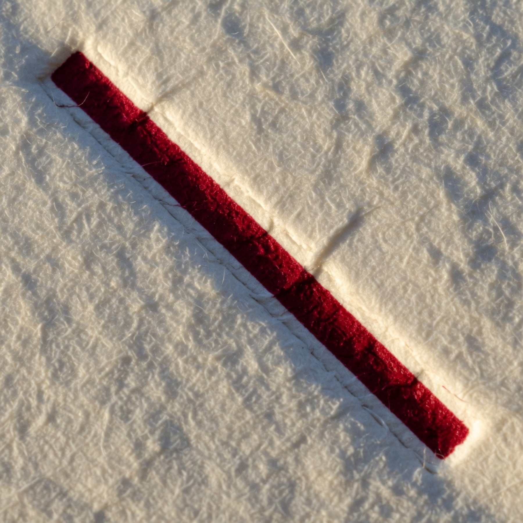 Close view of a crimson rule pressed into cotton paper.